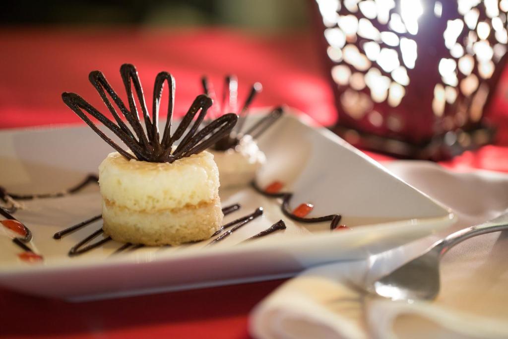 Dekoratīvs deserts ar krēmīgu pildījumu un šokolādes dekorācijām pasniegts uz baltas šķīvja, apkārt zīmēti šokolādes un ogu saucieni.