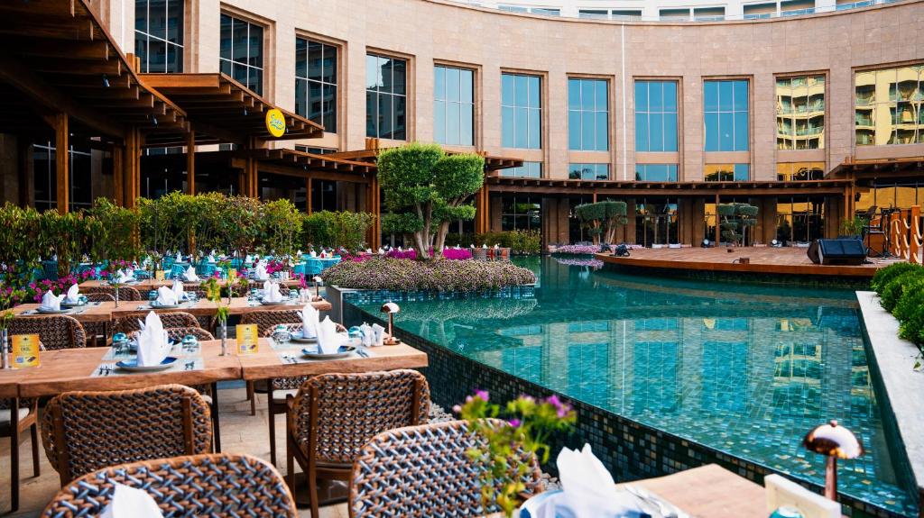 Kaya Palazzo Golf Resort āra ēdamzona pie baseina ar ziediem un koka terasi.
