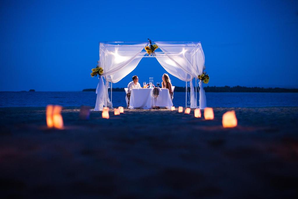 Romantisks vakariņu galds pludmalē ar sveču apgaismojumu un balto telti zem zvaigžņotām debesīm. Ideāla atmosfēra romantiskām reizēm.