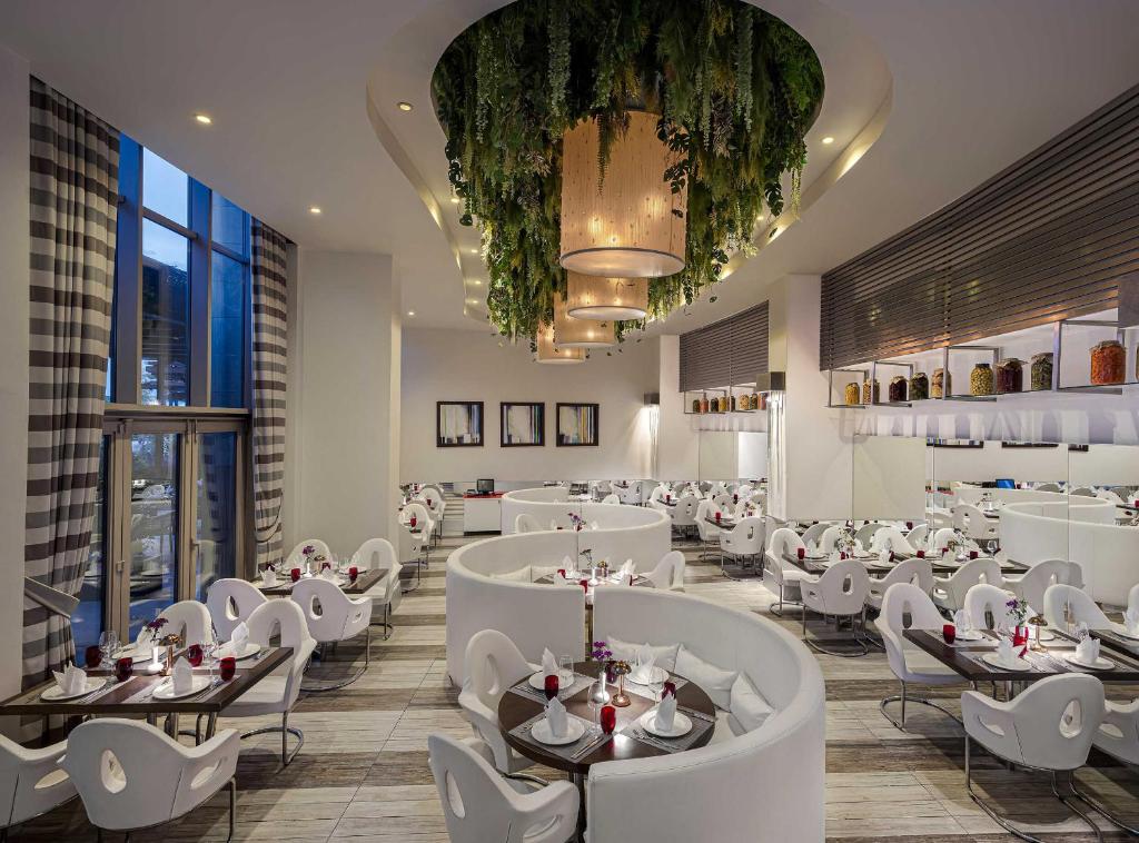 Mūsdienīgs restorāns Kaya Palazzo Golf Resort ar elegantiem galdiem un zaļumiem
