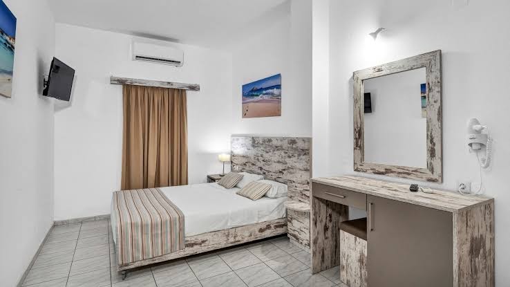 Evina Rooms & Suites gaišs guļamistabas numurs ar divguļamo gultu, koka mēbelēm, spoguli un gaisa kondicionieri Krētā