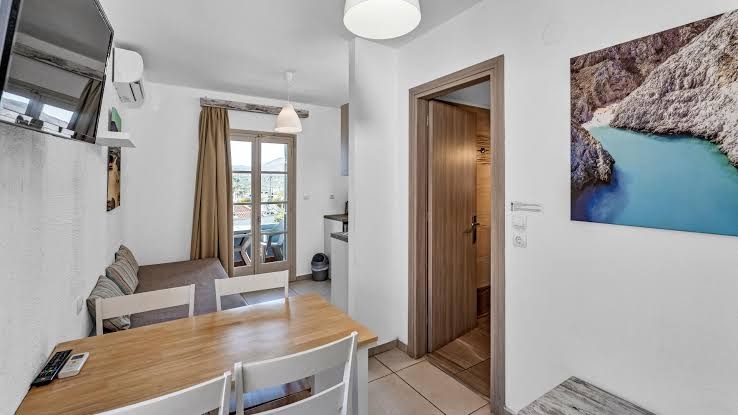 Evina Rooms & Suites numura interjers ar koka ēdamgaldu, dīvānu un skatu uz balkonu caur stikla durvīm