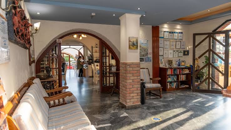 Evina Rooms & Suites mājīgais lobby un uzņemšanas zonas interjers ar dīvāniem, grāmatu plauktu un tradicionāliem dekoru elementiem Krētā