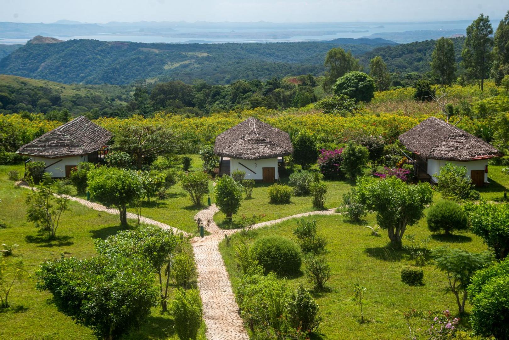 Vairāki mazi bungalo ar salmu jumtiem zaļā dārzā piekrastē.
