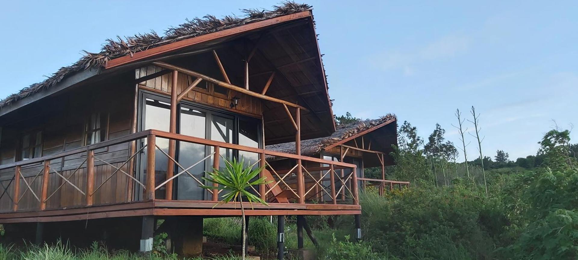 Divi koka bungalo uz pāļiem ar skatu uz zaļo apkārtni.