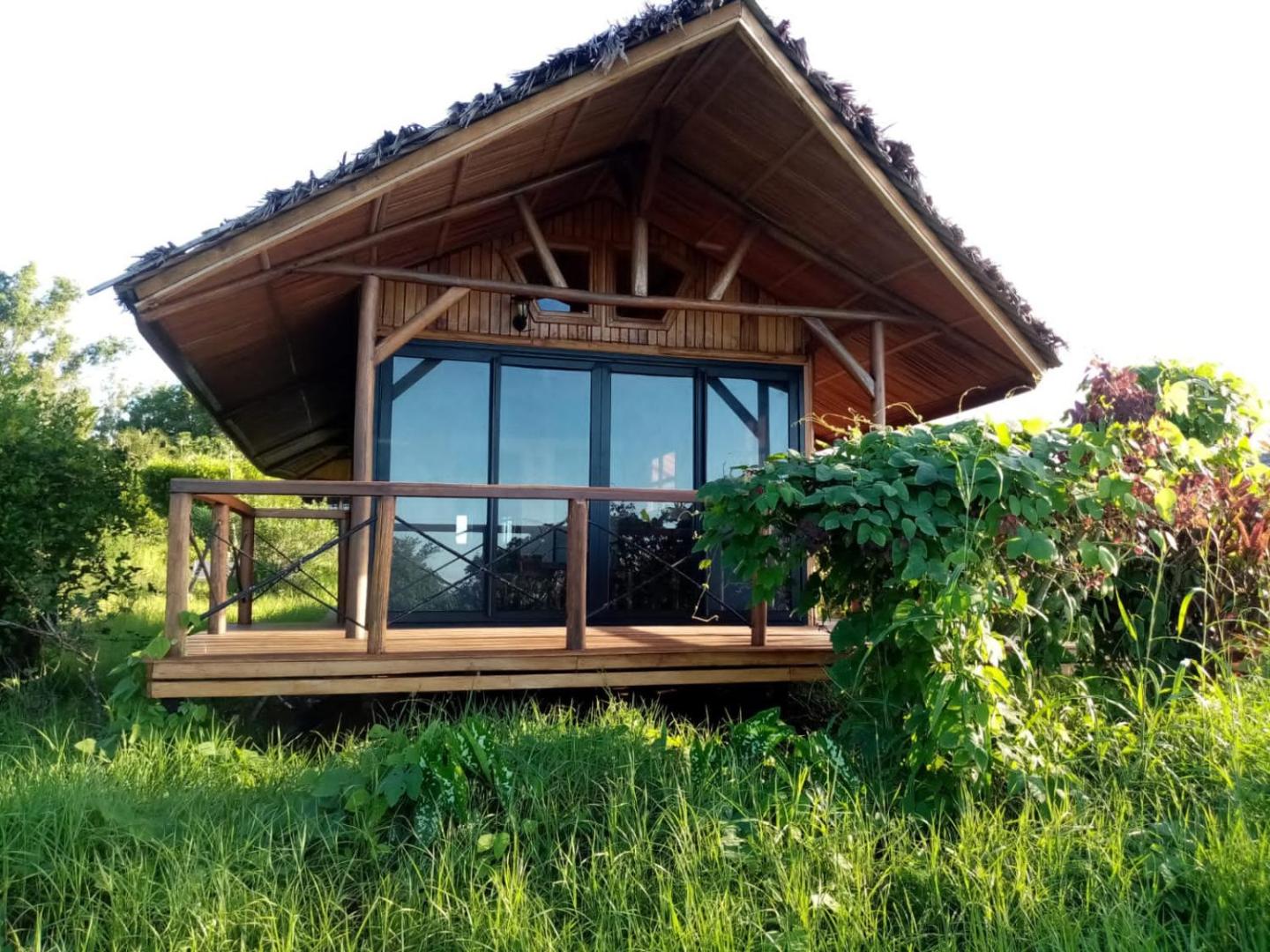 Koka bungalo ar stikla durvīm un terasi, ko ieskauj zaļa zāle.