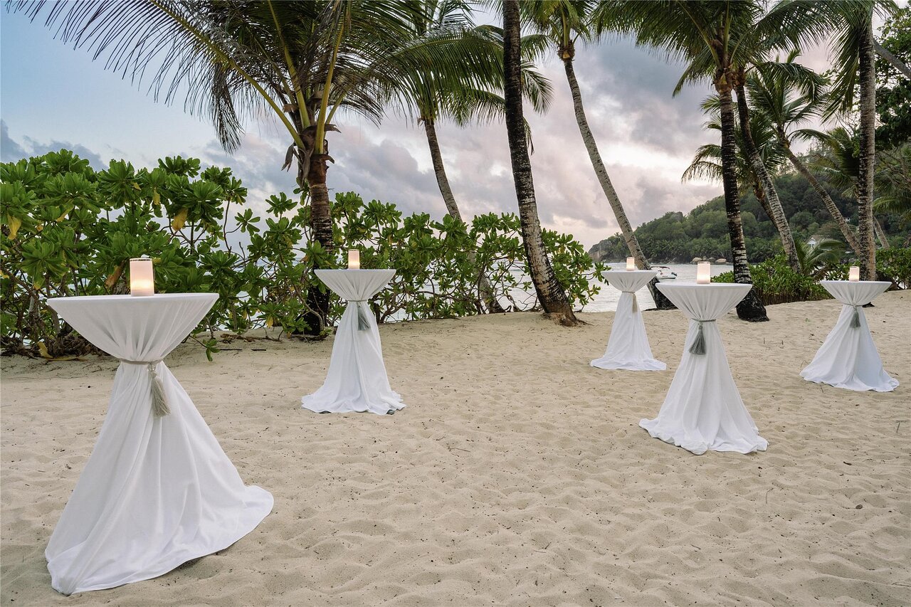 Kempinski Seychelles Resort pludmales zona ar elegantiem, baltiem kokteiļu galdiem un svecēm