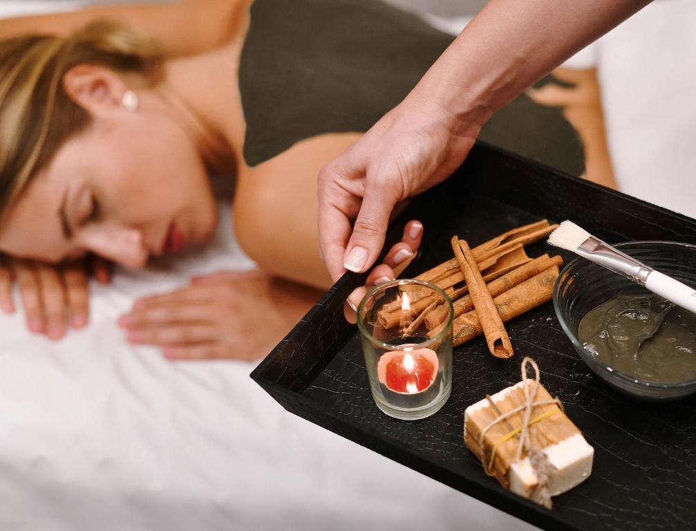 Masāžas sesija ar aromātiskām sastāvdaļām, tostarp kanēli, sveci un dabiskiem produktiem. Klientu relaksācija un labsajūta ir galvenais mērķis.