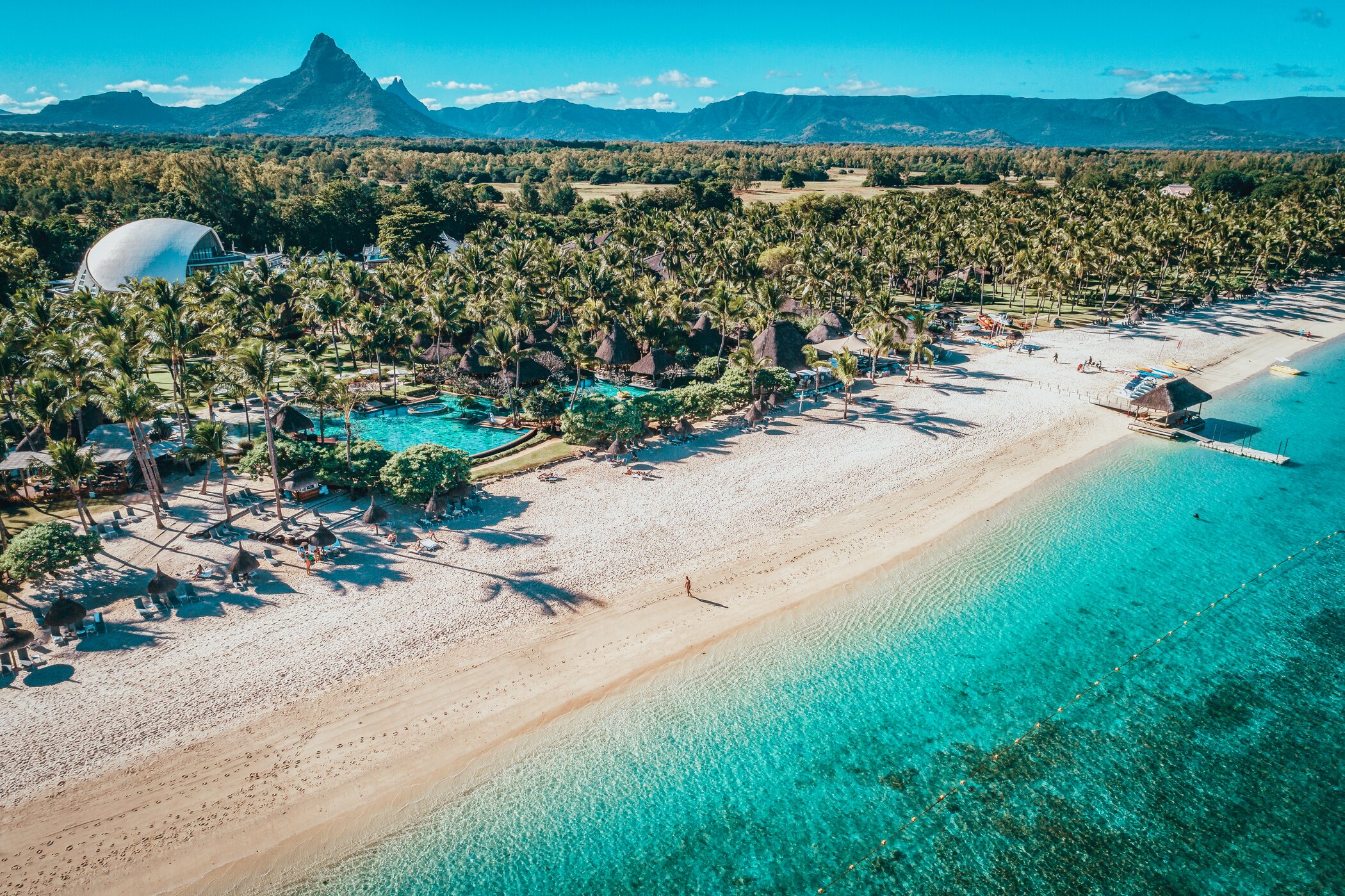 Skaista pludmale ar palmām un skaidru ūdeni, fons ar kalniem un viesnīcu kompleksu. Ideāla brīvdienu ainava. panoramic view with beach and pools