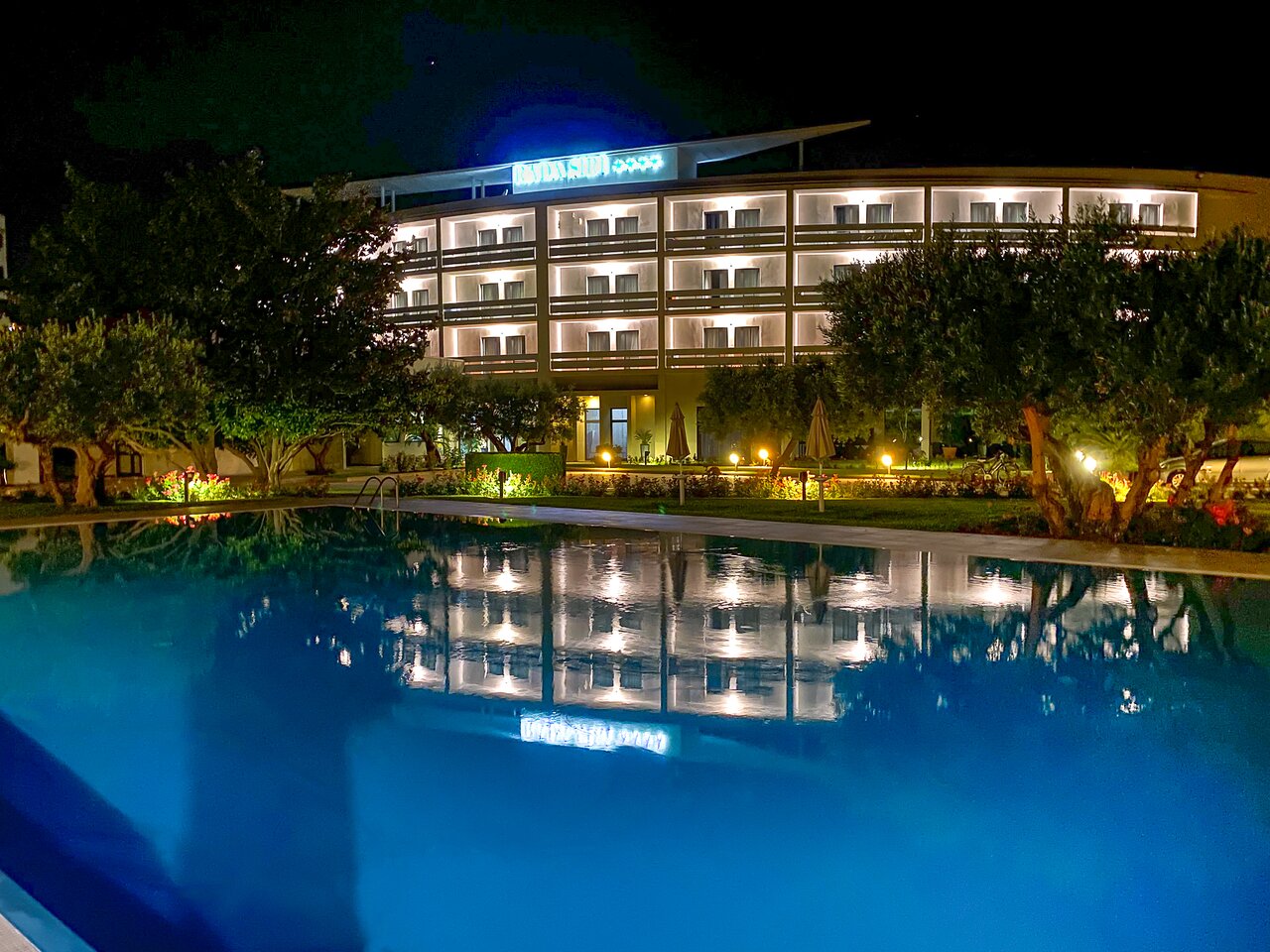 Rada Siri Hotel nakts skatā ar apgaismotu baseinu priekšplānā.