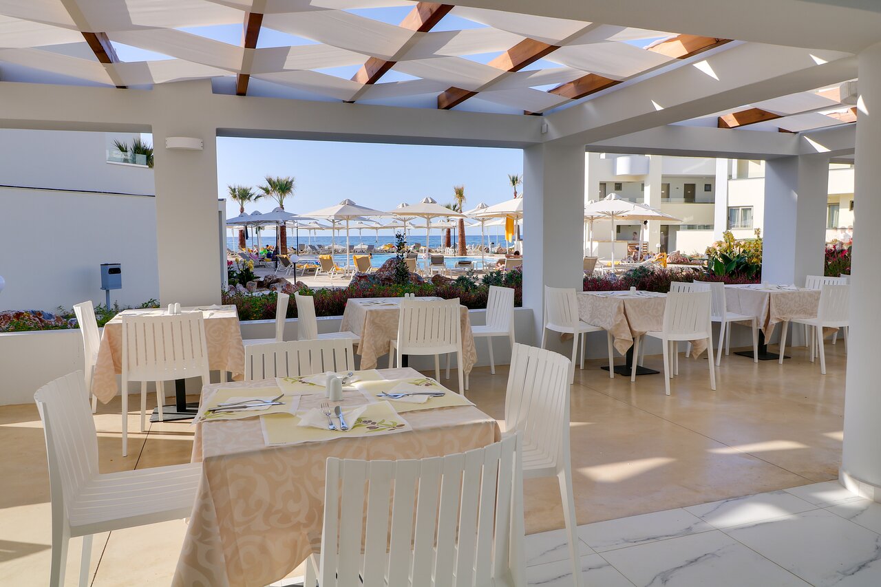Harmony Rethymno Beach āra restorāna terase ar galdiņiem un skatu uz baseinu un jūru