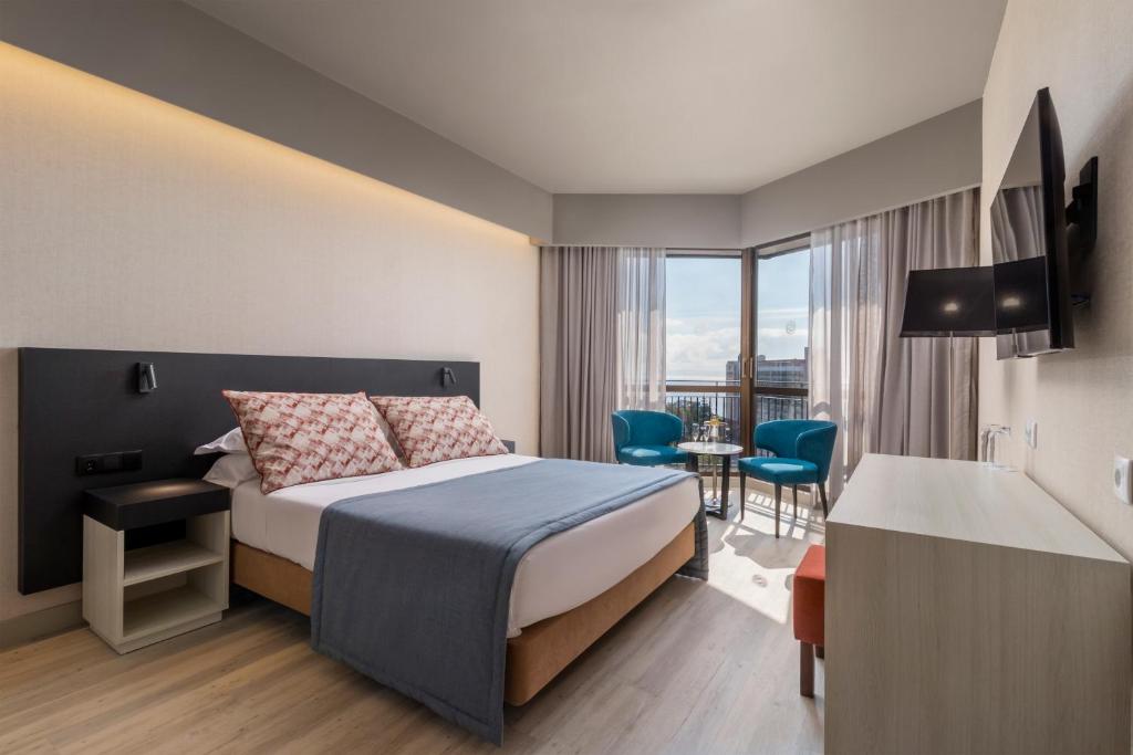 Mūsdienīga viesnīcas numura interjers ar divguļamo gultu, ērtām krēslām un skatu uz pilsētu. Numurā ir televizors un gaišas logu žalūzijas.