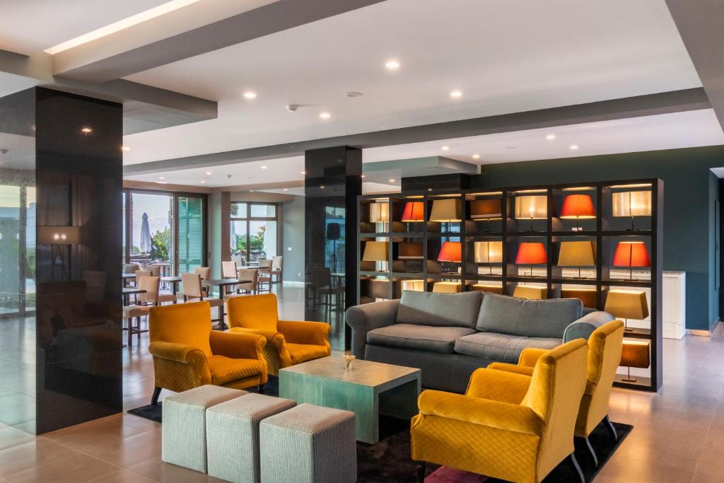 Mūsdienīgs viesnīcas viesistabas interjers ar dzeltenām un pelēkām mēbelēm, stilīgu apgaismojumu un plašām logu daļām, kas nodrošina dabīgu gaismu.