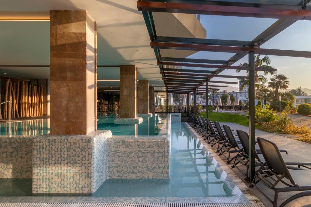 Mūsdienīga spa zona ar baseinu, kas iekārtota ar flīzēm un koka elementiem, kā arī atpūtas krēsliem, kas izvietoti zem nojumes. Apkārtne ir zaļa un sakopta, radot relaksējošu atmosfēru.