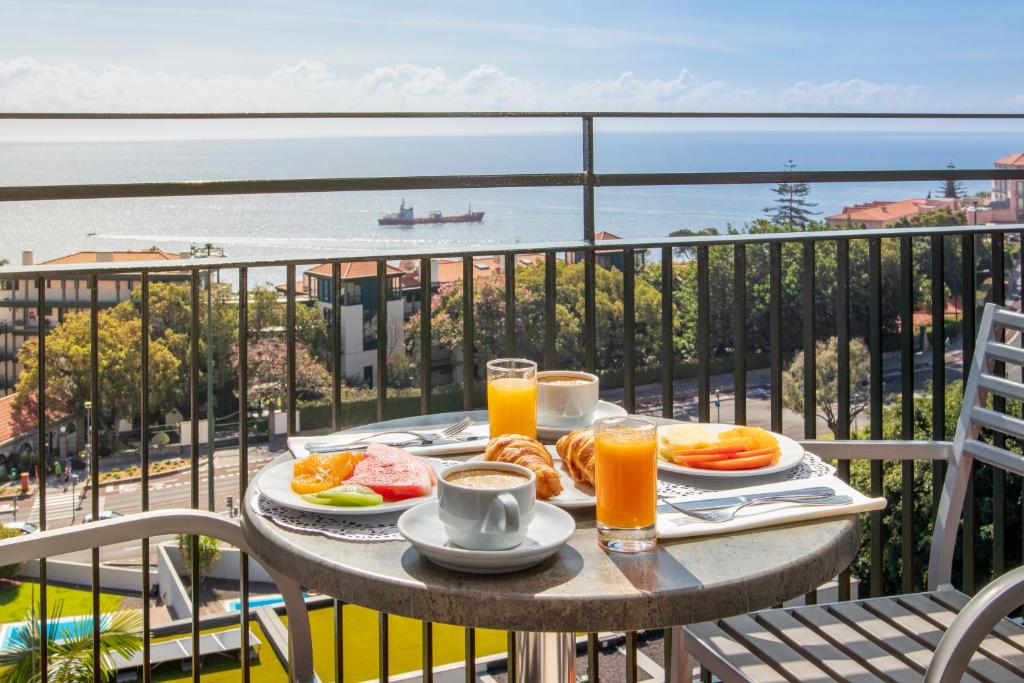 Broka ar augļiem un dzērieniem, baudot skatu uz jūru. Galda klājs ar kafiju, sulām un kruasāniem.