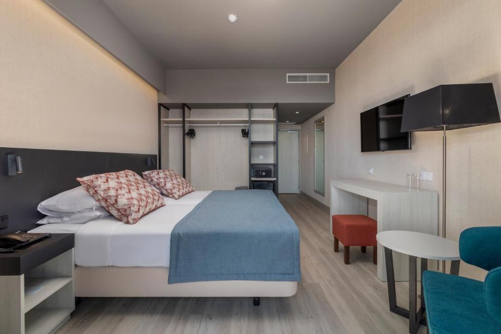 Mūsdienīga viesnīcas istaba ar divguļamo gultu, dekoratīviem spilveniem un ērtiem krēsliem. Interjers ir gaišs un minimālists, ar koka grīdu un modernām mēbelēm.