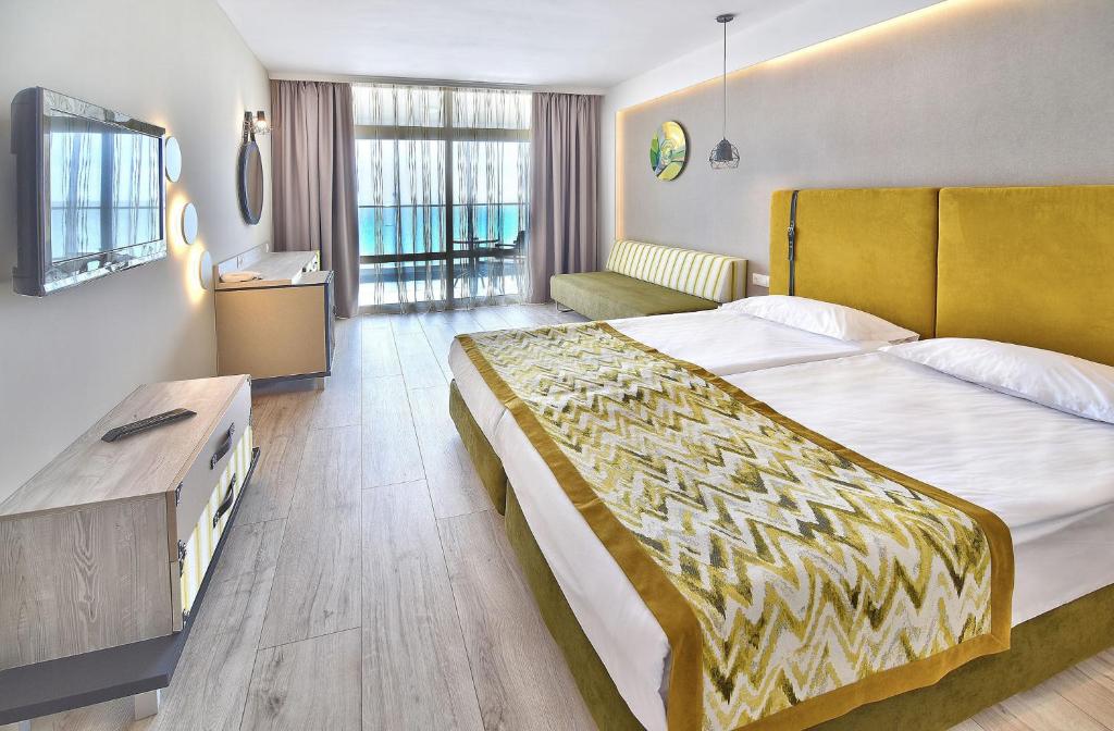 Mūsdienīga viesnīcas numura interjers ar divguļamo gultu, dīvānu un televizoru. Lielie logi nodrošina daudz gaismas un skatu uz ārpusi.