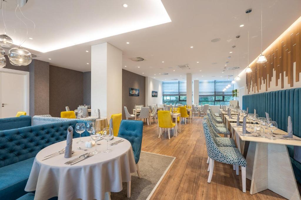 Mūsdienīgs restorāna interjers ar stilīgām mēbelēm, zilām un dzeltenām krēslēm, kā arī eleganti klātiem galdiem. Gaisma ir maiga un telpa ir plaša, radot patīkamu atmosfēru.