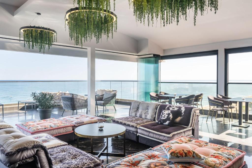 Mūsdienīgs interjers ar panorāmas skatu uz jūru, kurā redzami ērti dīvāni un stilīgas gaismas. Telpa ir gaiša un viesmīlīga, ideāla relaksācijai un socializēšanai.