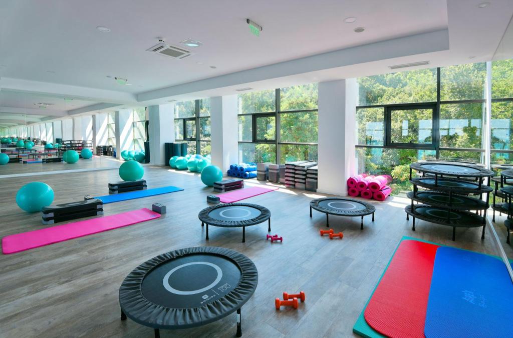 Mūsdienīga trenažieru zāle ar dažādiem fitnesa aprīkojumiem, tostarp trampolīniem, vingrošanas bumbām un paklājiem, kas nodrošina lielisku vidi aktīvai nodarbībai. Lielie logi ļauj ieplūst dabīgai gaismai un piedāvā skatu uz dabu.