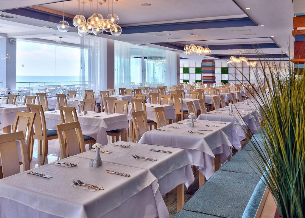 Lielas un modernas restorāna telpas ar baltām galdautām un koka krēsliem, kas piedāvā skatu uz jūru. Apgaismojums ir mūsdienīgs, radot patīkamu atmosfēru.