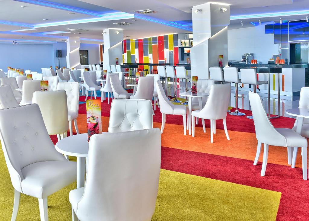 Mūsdienīgs kafejnīcas interjers ar baltām krēslu un galdu kombinācijām, ko papildina spilgti krāsains paklājs un stilīgs bārs. Ideāla vieta relaksācijai un socializācijai.