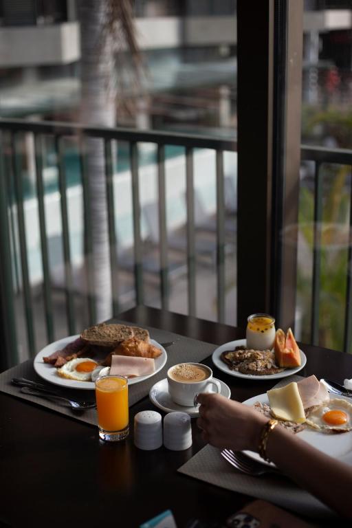 Brokastis ar olu, maizi un augļiem, papildinātas ar kafiju un sulu, baudītas pie loga ar skatu uz baseinu.