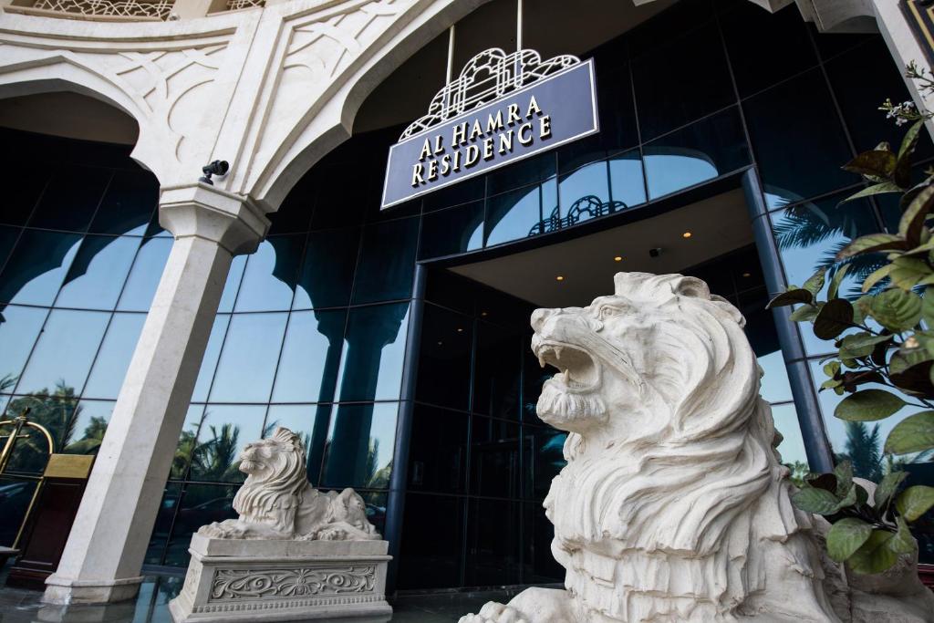 Al Hamra Residence ieeja ar diviem akmens lauvām, kas simbolizē greznību un viesmīlību. Modernā arhitektūra un spoguļojošie logi piešķir elegantu izskatu.