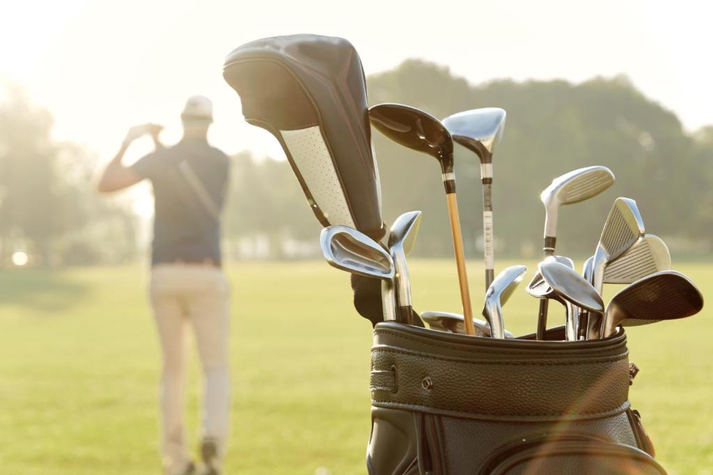 Golfu somas tuvumā ir dažādi golfa klubi, kamēr spēlētājs praktizē savu sitienu saulainā laukumā.