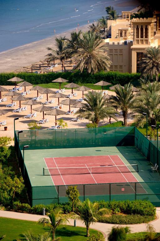 Tennis courts at a luxury resort, surrounded by palm trees and beach umbrellas, with a stunning ocean view.