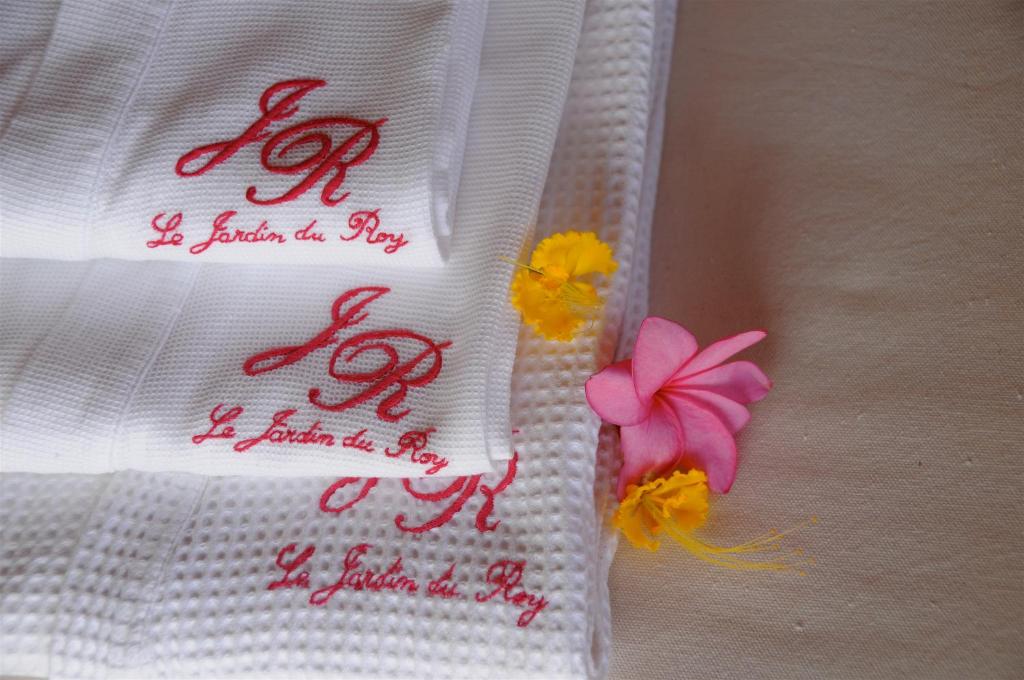 Balti dvieļi ar Le Jardin du Roy logo un ziediem.