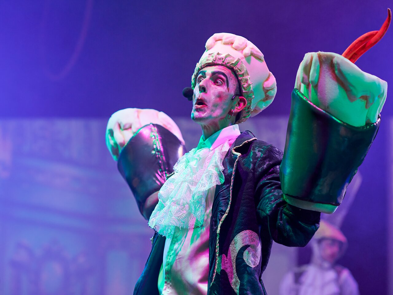 Klauns ar spilgtu tērpu uzstājas uz skatuves.