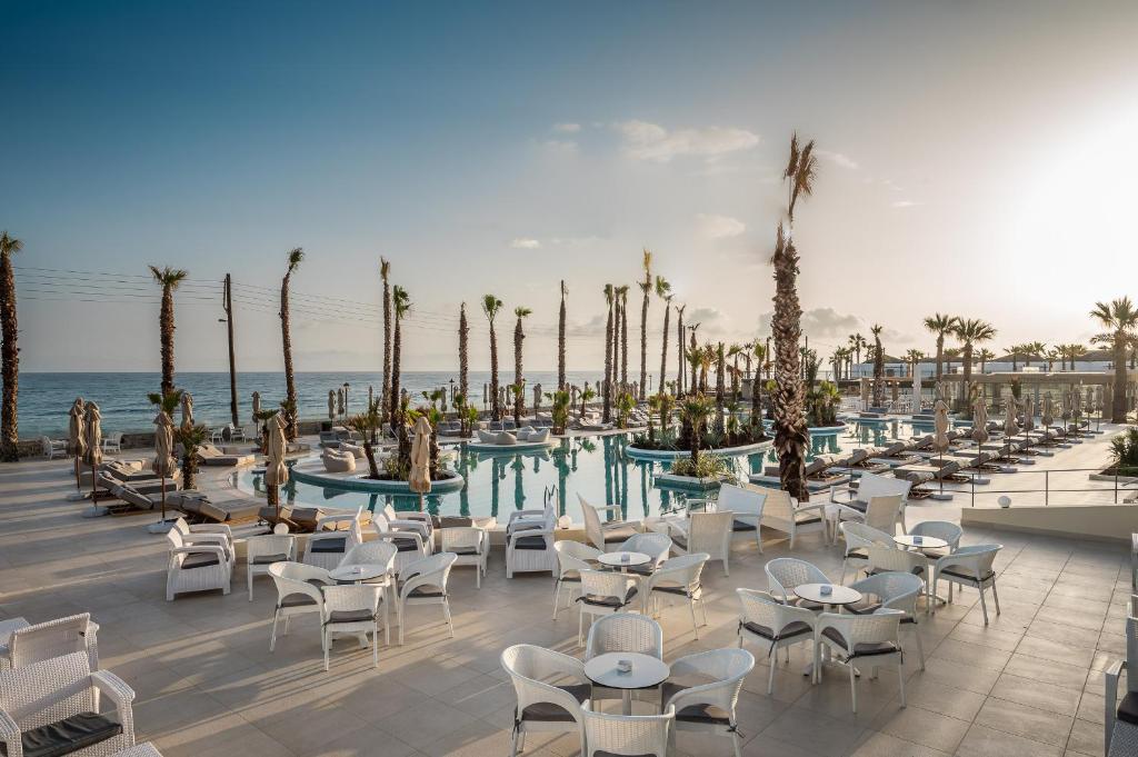 Luksusa viesnīcas peldbaseins ar palmām un sauļošanās krēsliem, kas atrodas pie jūras. Ideāla vieta relaksācijai un atpūtai saulainā dienā.