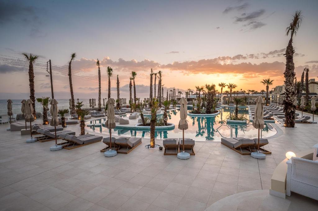Mūsdienīgs kūrorts ar baseinu un palmām, kas atrodas pie jūras, ar saulrietu fona. Ideāla vieta relaksācijai un atpūtai.