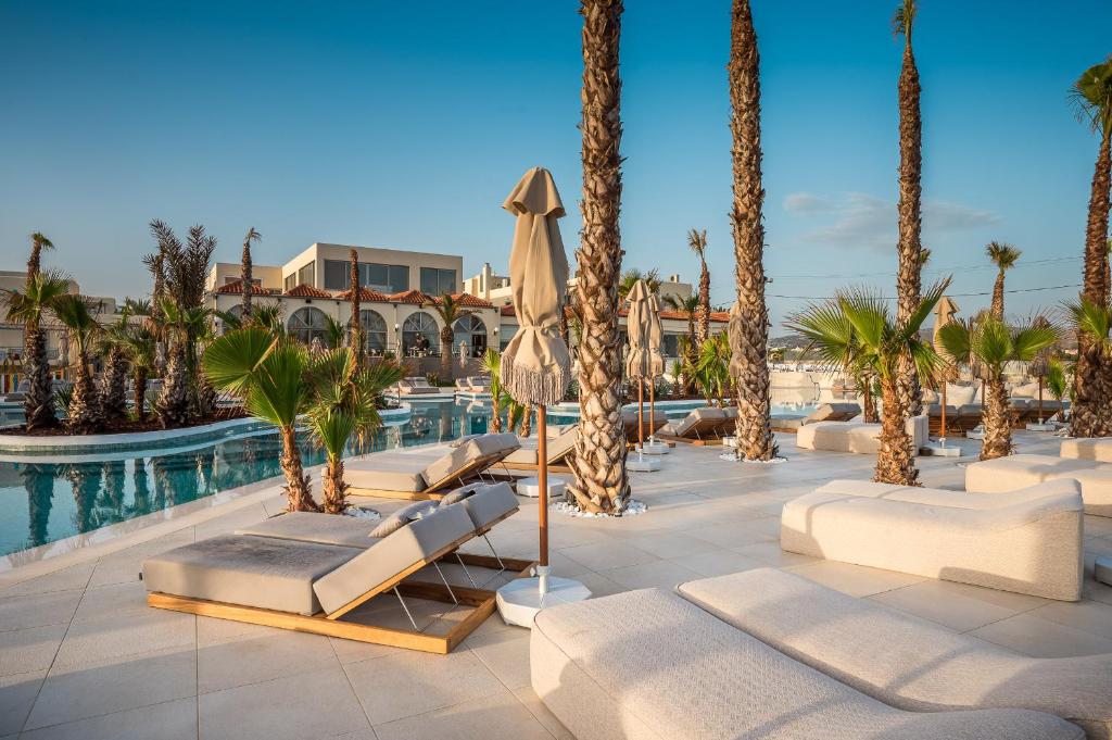 Luksusa viesnīcas baseins ar palmām un saulessargiem, kur ir ērti guļamkrēsli, nodrošina relaksējošu atpūtu saulainā dienā.