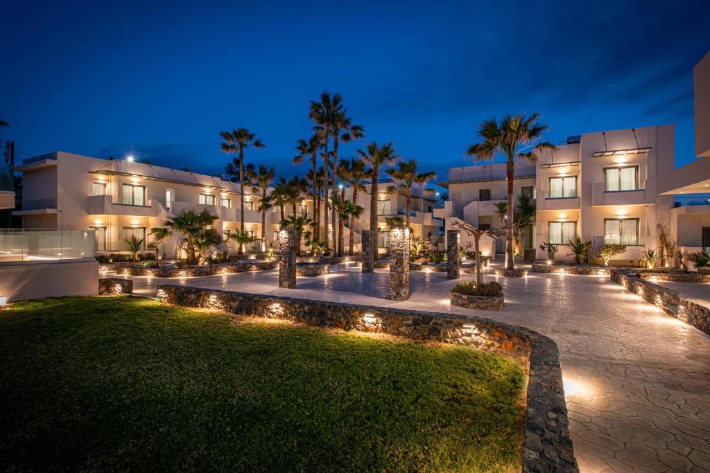 Saint George Gournes Bay viesnīca piekrastē tumsā ar apgaismotu dārzu.