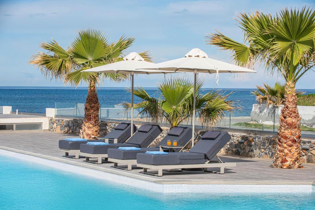 Viesnīcas Saint George Gournes Bay baseins ar saulessargiem un palmām piekrastē.