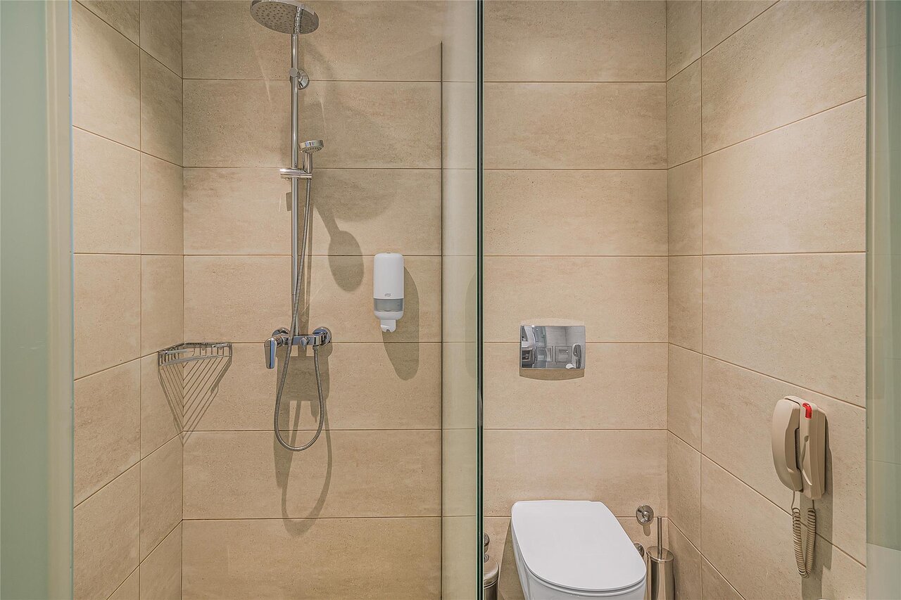 Panorama Village Hotel numura vannas istaba ar dušas kabīni un gaišu flīžu apdari.