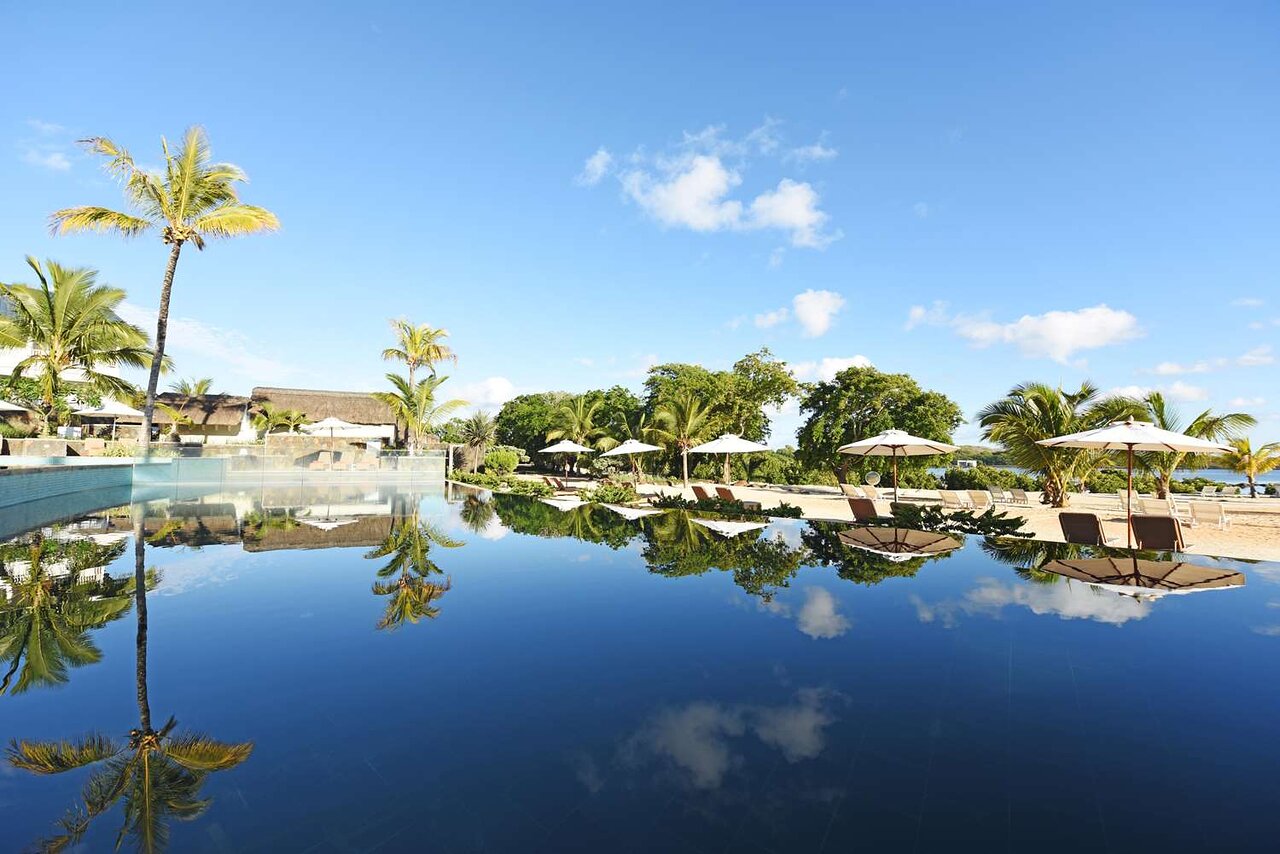 Luksusa viesnīcas baseins ar palmām un sauļošanās krēsliem, atspoguļojot debesis un dabu. Ideāla atpūtas vieta tropiskā vidē. panoramic view with beach and pools