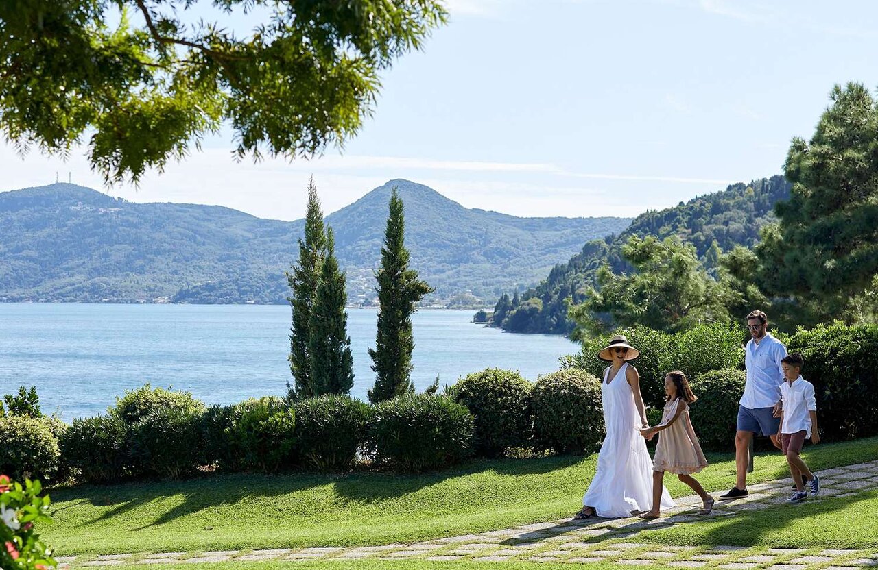Ģimene pastaigā pa skaistu ainavu ar ezeru un kalniem fona. Saulaina diena ar zaļu zālienu un kokiem apkārt. panoramic view with beach and pools