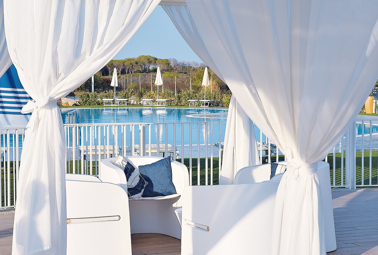 Janna 'e Sole Resort atpūtas nojume ar baltiem aizkariem un skatu uz saulaino peldbaseinu.