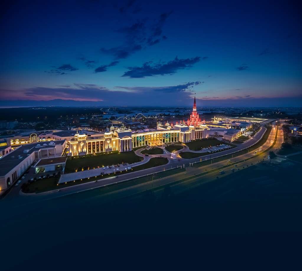 Apspīdēta pilsētas ainava ar modernām ēkām un ceļiem, kas ved uz spilgti apgaismotām struktūrām, kas atspoguļo nakts debesu krāsas. panoramic view with beach and pools