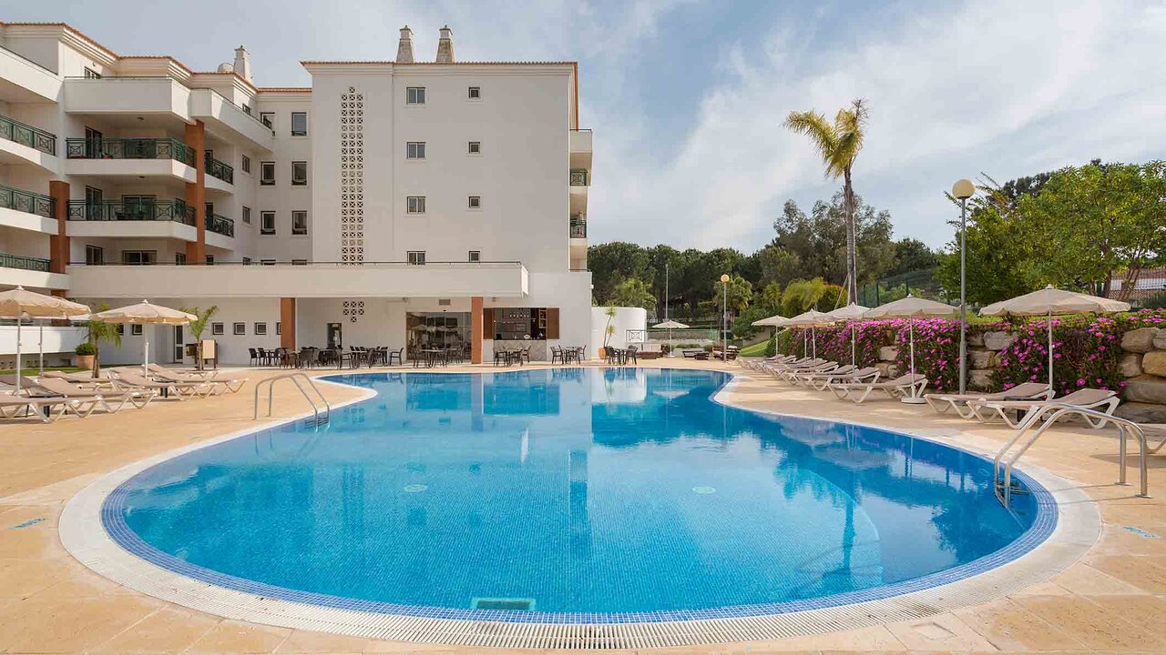 AP Victoria Sport & Beach Hotel āra peldbaseins ar sauļošanās krēsliem un balto viesnīcas ēku fonā.