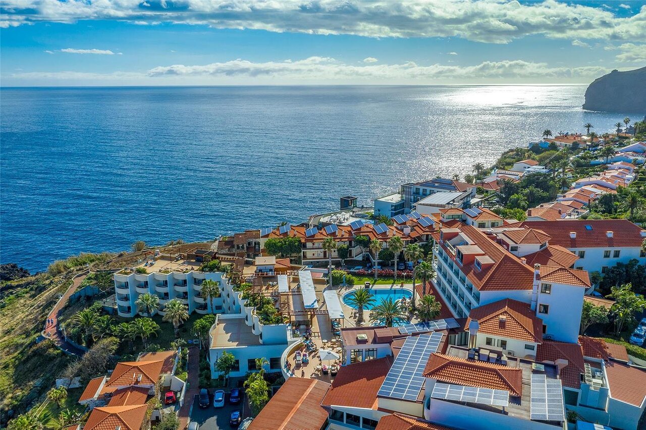 Kopskats uz piejūras kūrortpilsētu ar baseinu un mājām, kas izvietotas pakalnā. Zilā jūra un debesis papildina ainavu. panoramic view with beach and pools