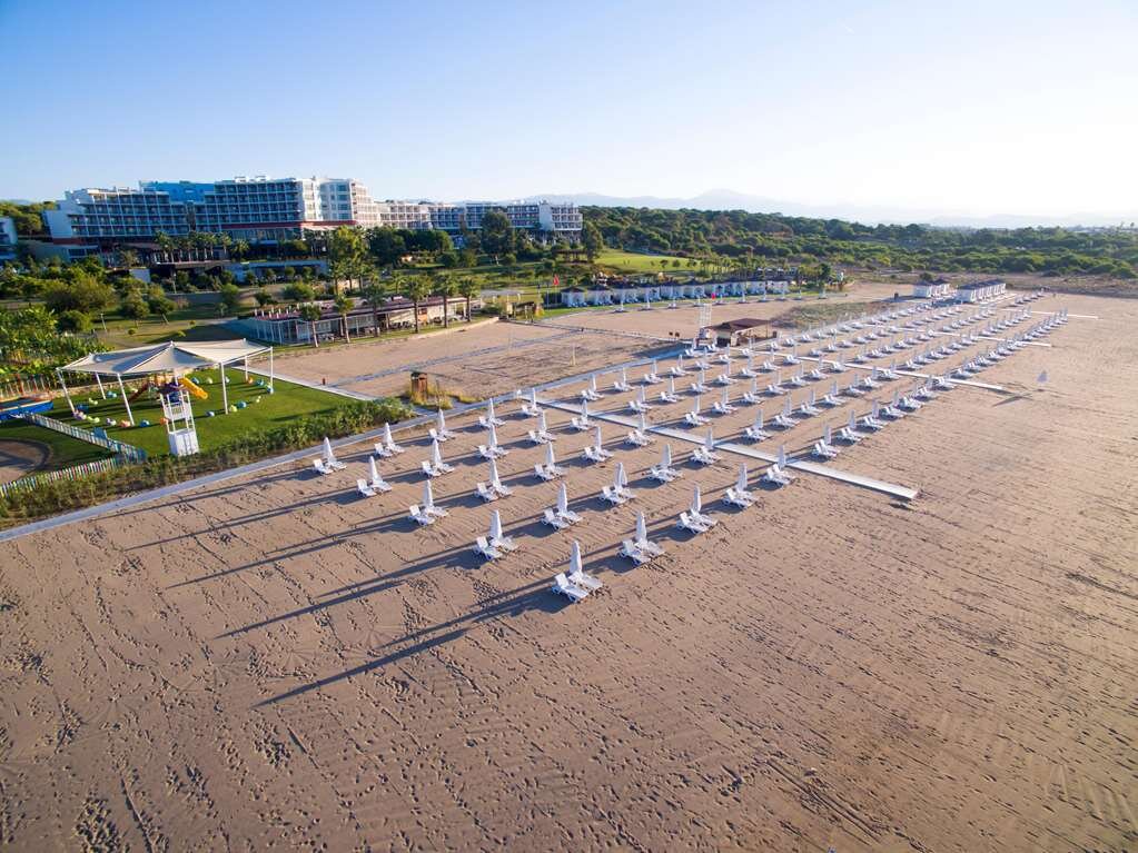 Pludmales skats ar baltiem saulessargiem, kas sakārtoti rindās, un viesnīcu fonā. Vieta ir ideāla atpūtai un ūdens sporta aktivitātēm. panoramic view with beach and pools