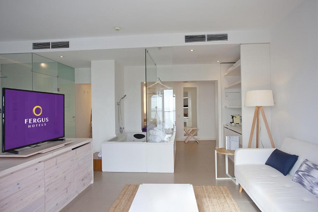 Mūsdienīgs viesnīcas numurs ar stikla dušu, baltu dīvānu un televizoru ar "Fergus Hotels" logotipu. Interjers ir gaišs un elegants, radot komfortablu atmosfēru.
