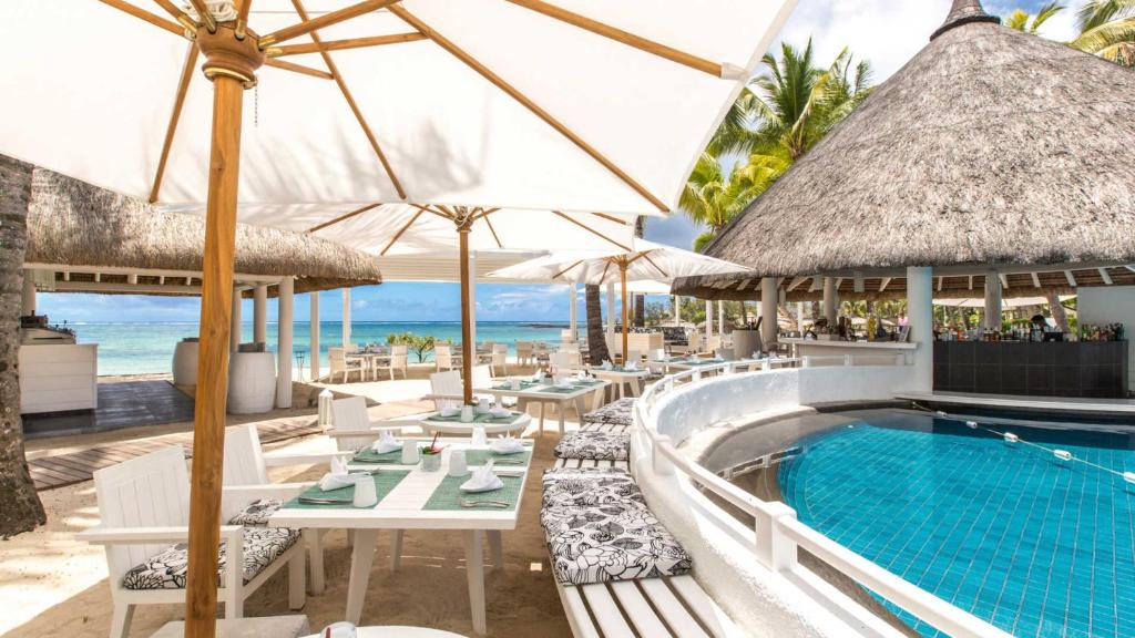 Pludmales restorāns ar peldbaseinu un saulessargiem, izceļoties ar tropisku atmosfēru un skatu uz jūru. Ideāla vieta relaksācijai un baudīšanai.