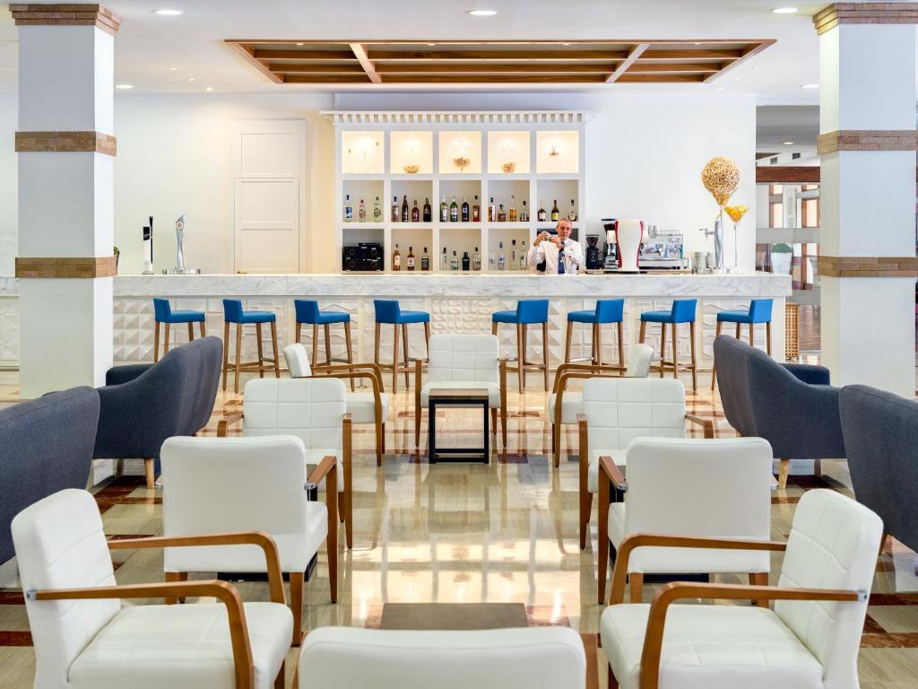 Mūsdienīgs bārs ar elegantiem krēsliem un stilīgu interjeru, kurā redzama dzērienu izvēle un apkalpojošs personāls. Ideāla vieta atpūtai un socializācijai.