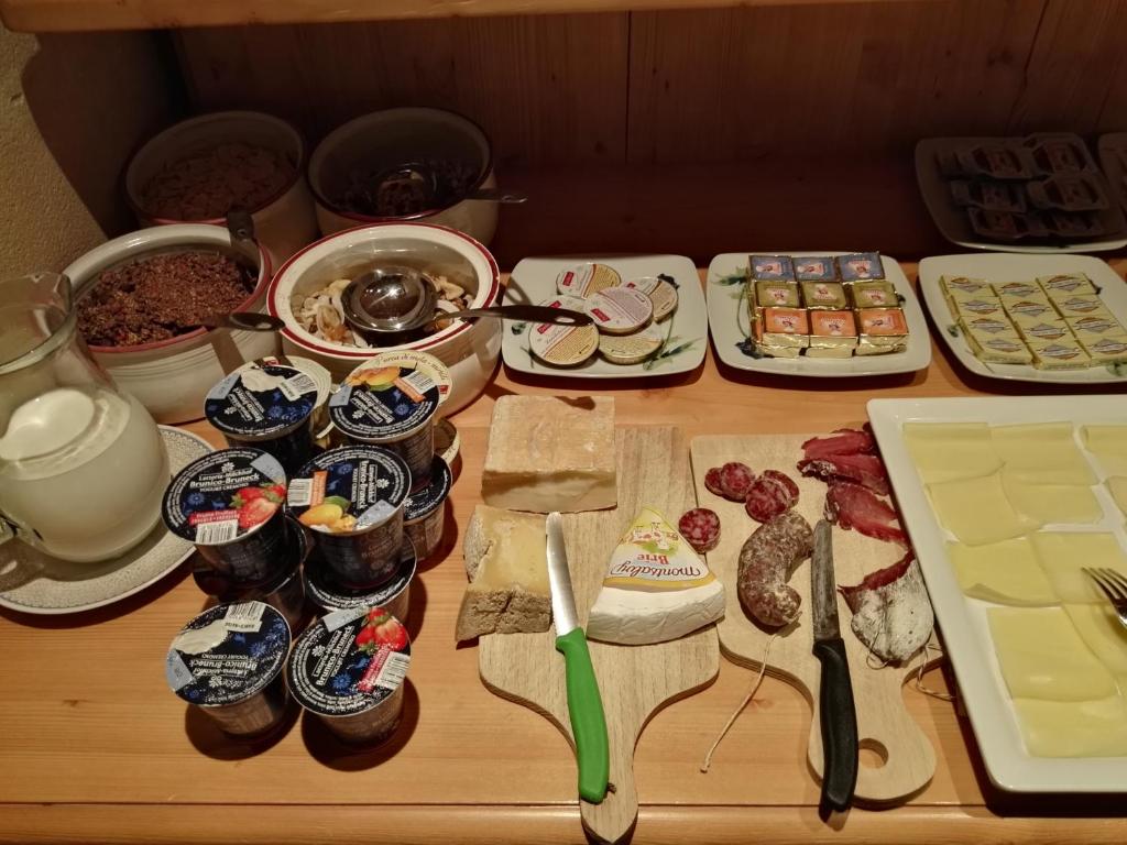 Bagātīgs brokastu galds ar jogurtu, sieriem, desām, graudaugiem un pienu, kas izkārtots uz koka virsmas. Ideāls izvēles klāsts, lai uzsāktu dienu.