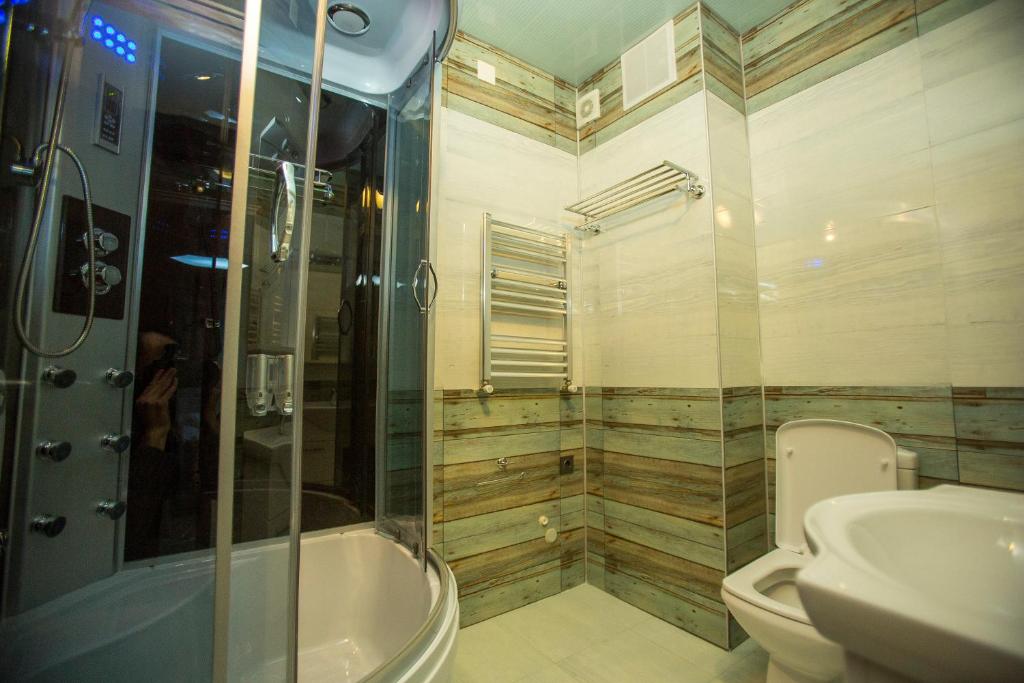 Mūsdienīgs vannas istabas interjers ar stikla dušu un modernu sanitāro tehniku. Sienas dekorētas ar koka apdari un keramikas flīzēm.